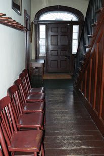 The front hall of Montgomery's Inn featuring dark wood and chairs that line the one wall.